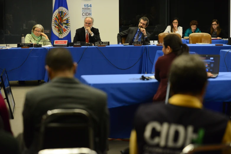 several people sitting at long tables in front of microphones