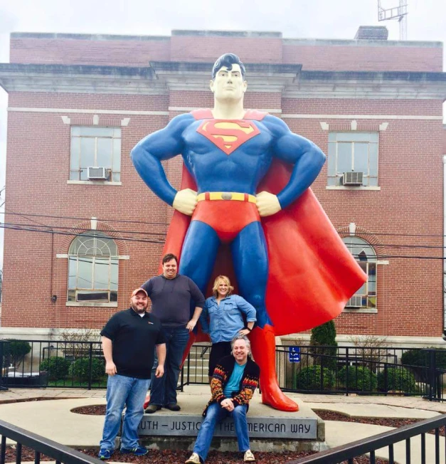some people standing in front of a statue of superman