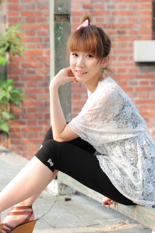 an asian woman sitting on a cement wall wearing black pants