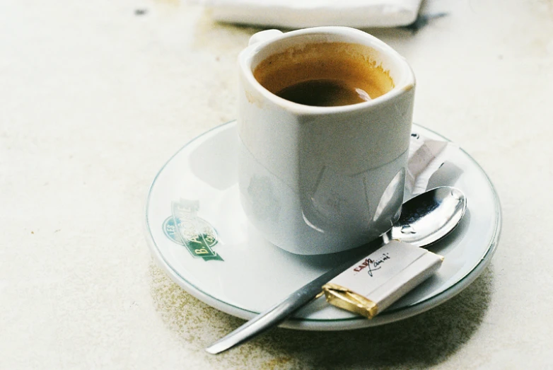 a cup of coffee next to a metal spoon on a plate