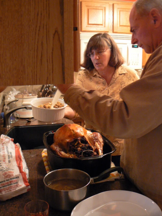 an older man and woman with pot roast chicken on the stove