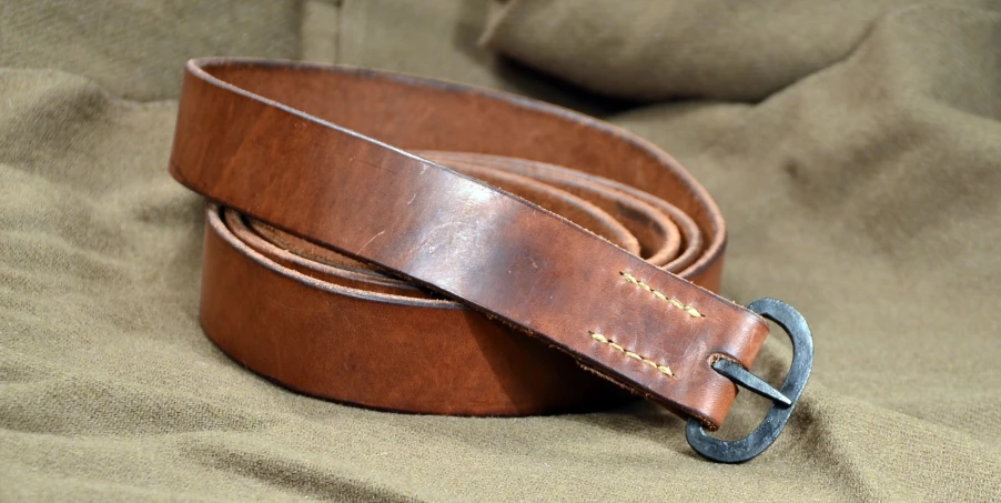 a brown belt with a metal buckle laying on a bed