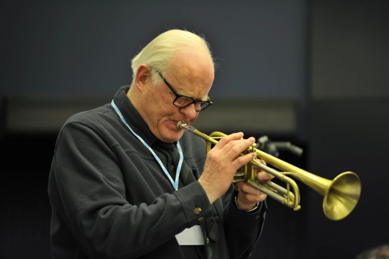 man with glasses plays his trumpet in front of a microphone