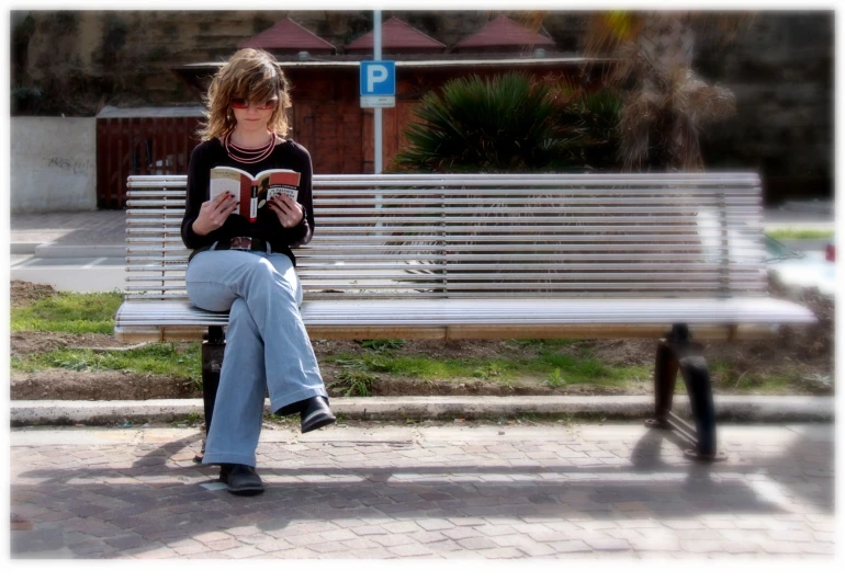 a girl sitting on a bench in front of a building reading a book