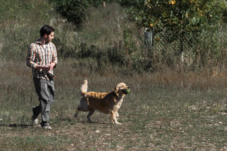 a man holding an apple in his mouth and walking with a dog