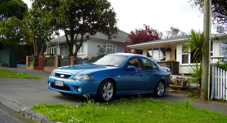 the blue car is parked in the grassy area beside the houses