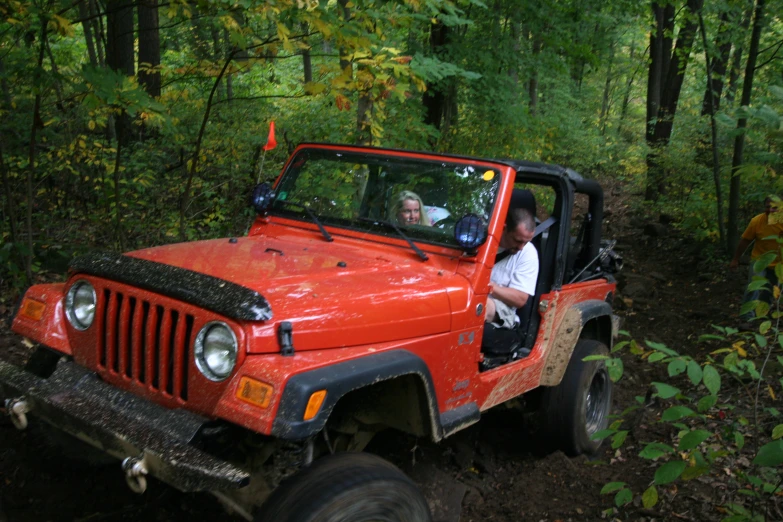 a man and a woman sitting in the drivers seat of an orange jeep