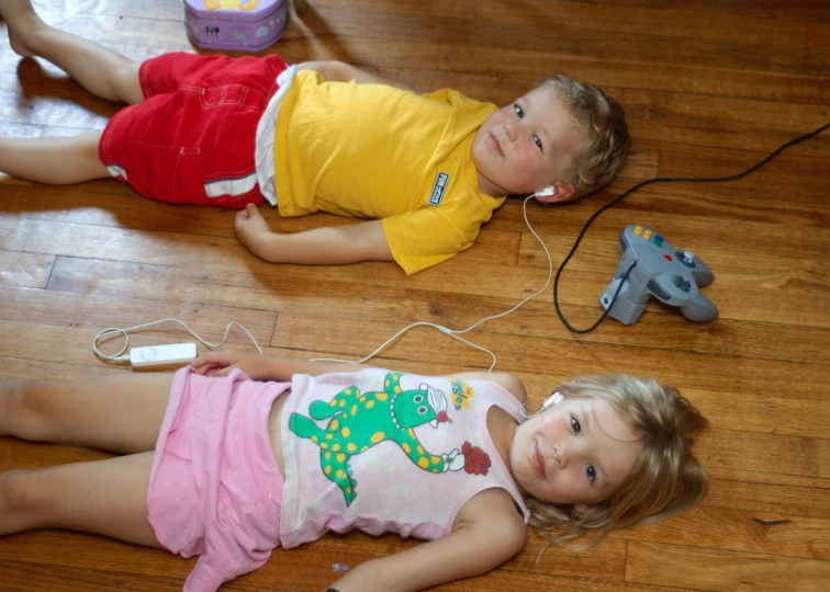 two children laying on the floor next to a wii controller