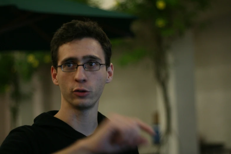 a young man in glasses stands near an open umbrella