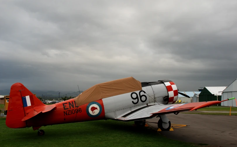 an old - fashioned plane on a patch of grass next to some barns