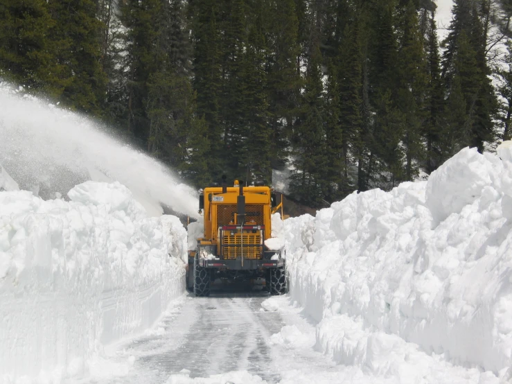 a large tractor spewing snow on the side of a road