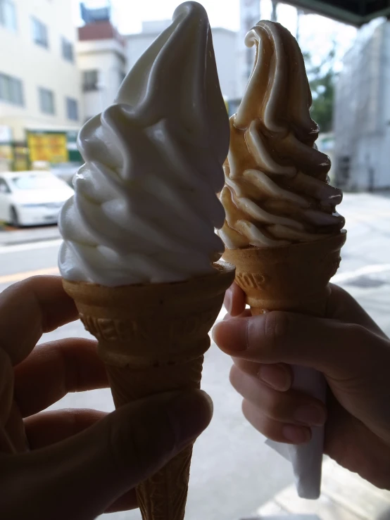 two people holding ice cream cones on a street