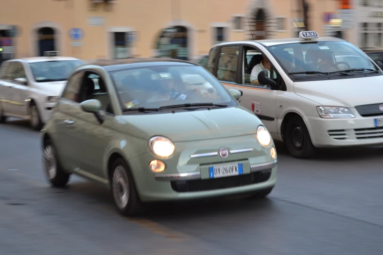 a green car driving on the street with a white van and another vehicle behind it