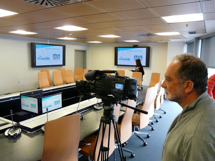 a man is standing in front of a camera at an empty desk