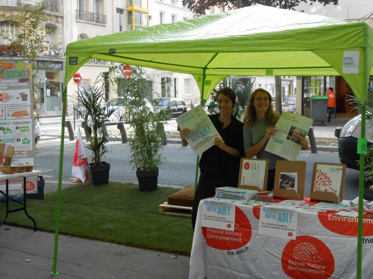 two women standing under a green tent holding up pieces of paper