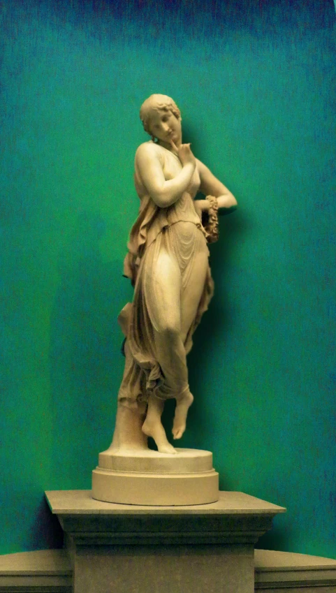 the statue of the woman is standing in front of the green wall