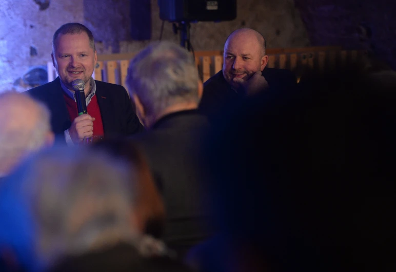 people sitting together at an event listening to someone on a cell phone