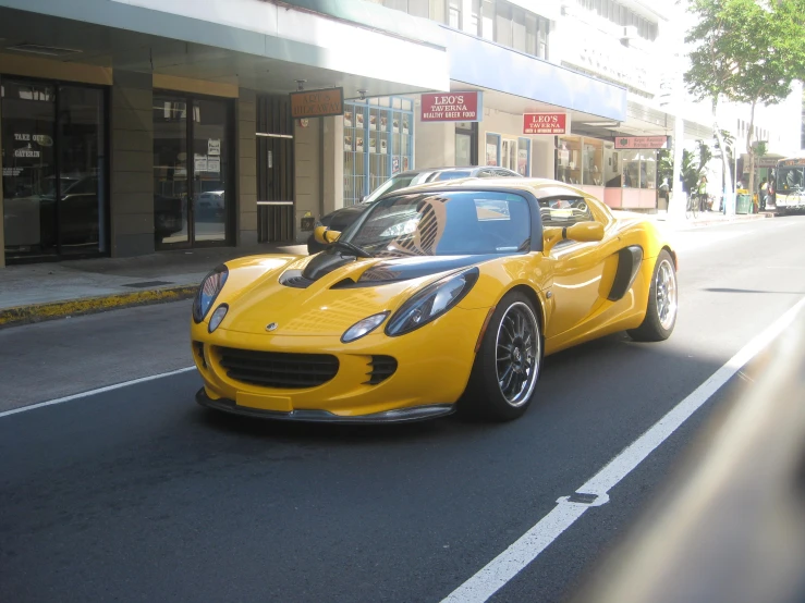 a yellow lotus car driving down a street