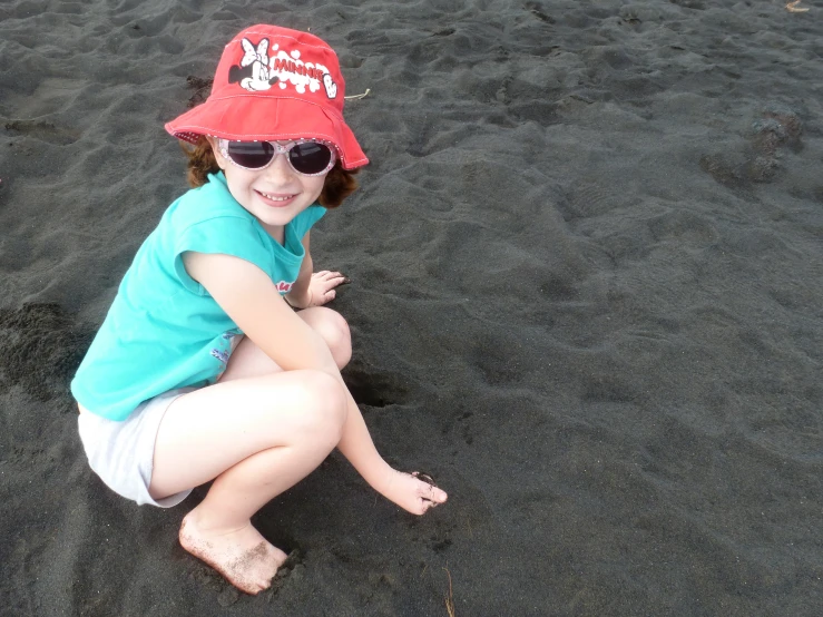 a child is sitting on the sand and wearing a hat