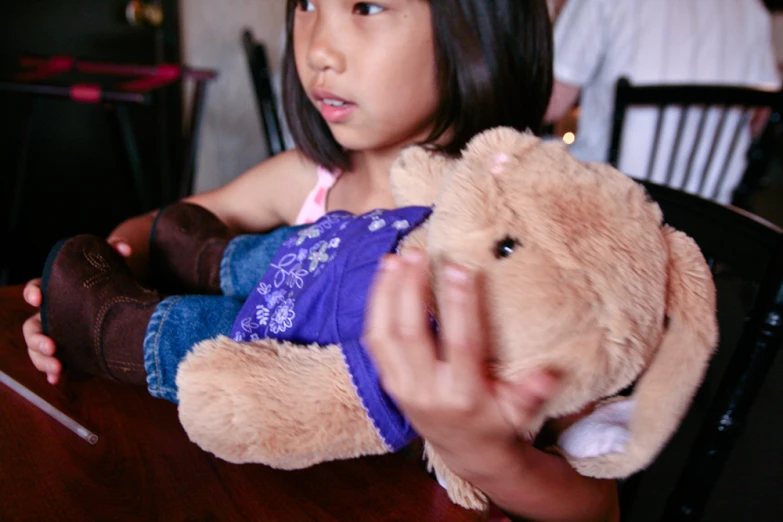 a little girl is sitting in a chair holding a large stuffed animal
