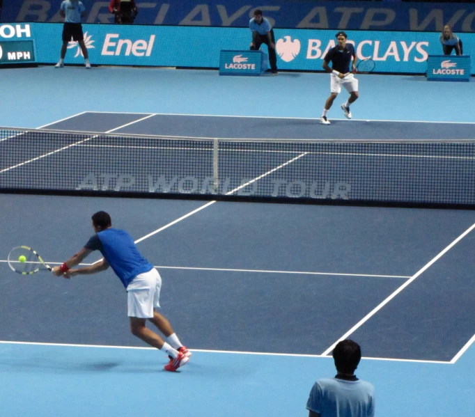 two men play doubles tennis on a blue court