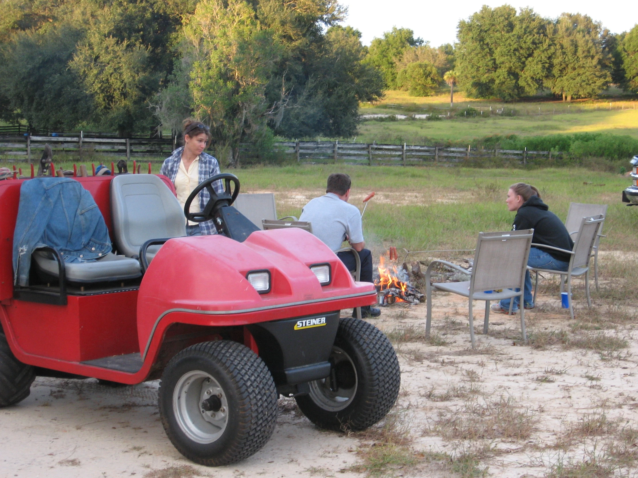 people gathered around a small red vehicle sitting on the sand