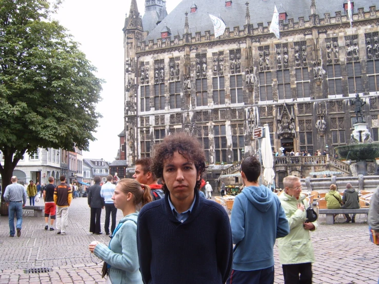 a young man stands with his hands together, looking at the camera