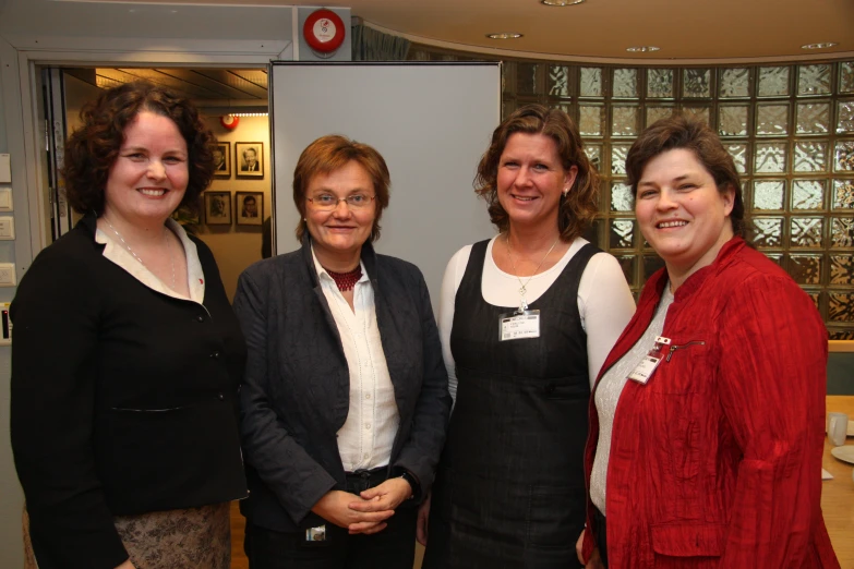 four woman smile at the camera in front of a window