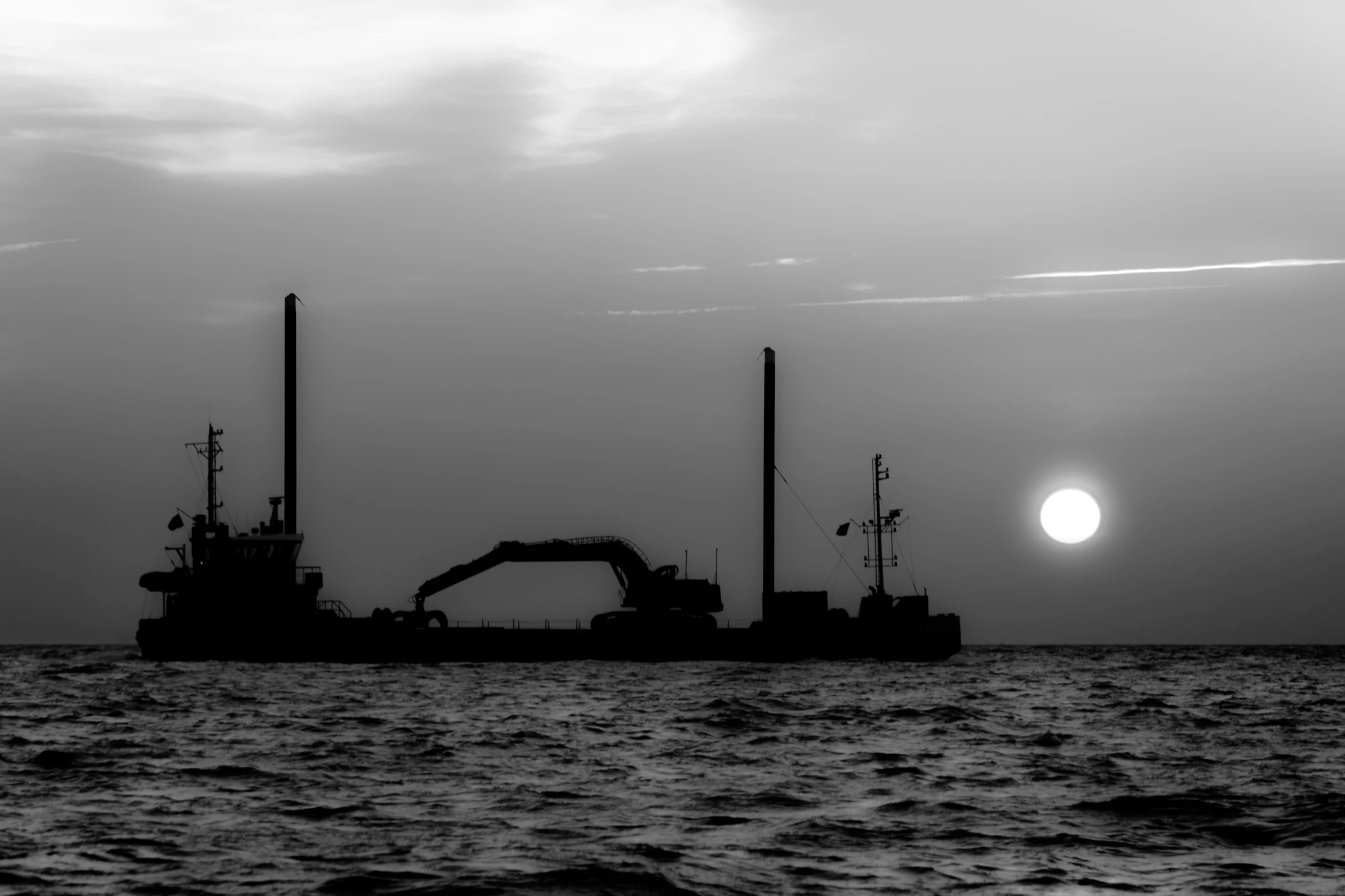 a silhouetted boat is out on the ocean by a full moon