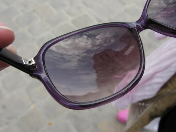 the reflection of a building and clouds on an extremely violet - tinted sunglasses