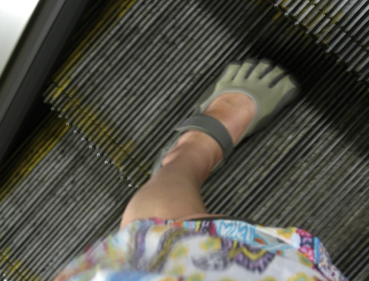 woman's bare feet wearing green rubber shoes, and patterned dress with patterned belt