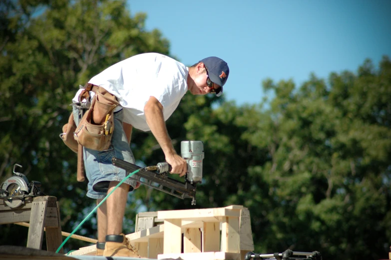 a man wearing a white shirt and shorts, using a nail gun and a water can