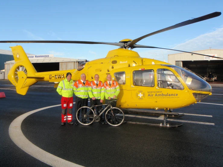 two men stand next to a yellow helicopter