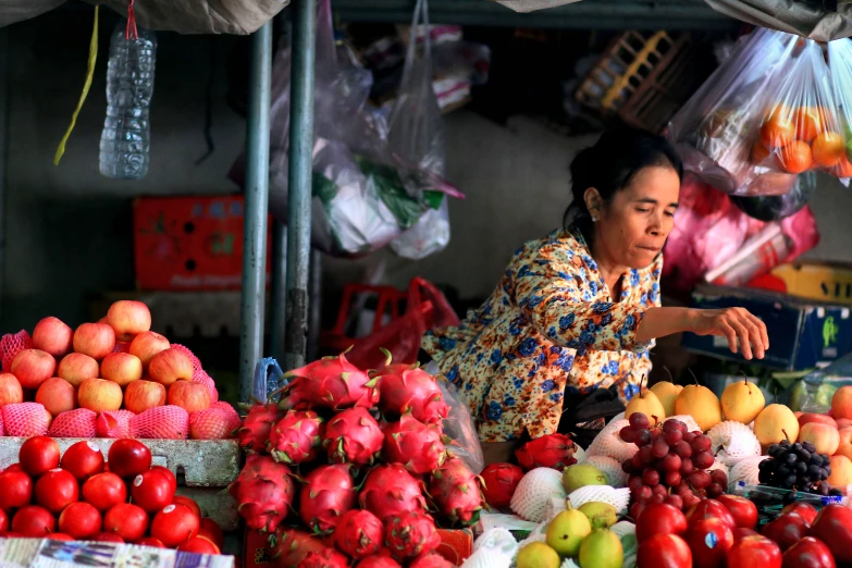 an asian woman at a fruit stand is purchasing some fruits