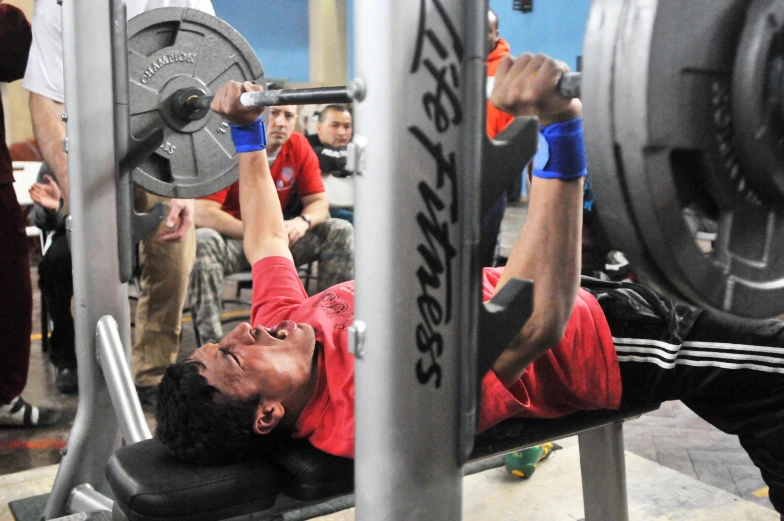 man lifting weights at a gym bench in front of an audience