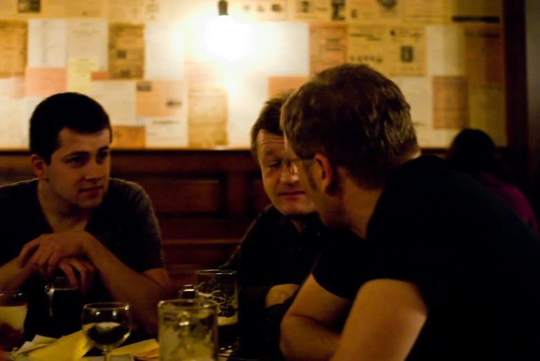 three men sit at a table having a discussion