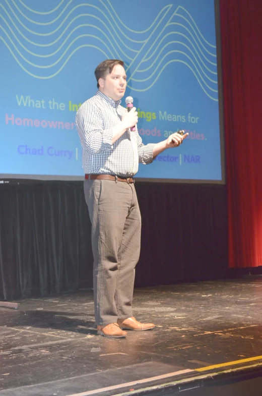 a man standing on stage in front of a projection screen giving a presentation