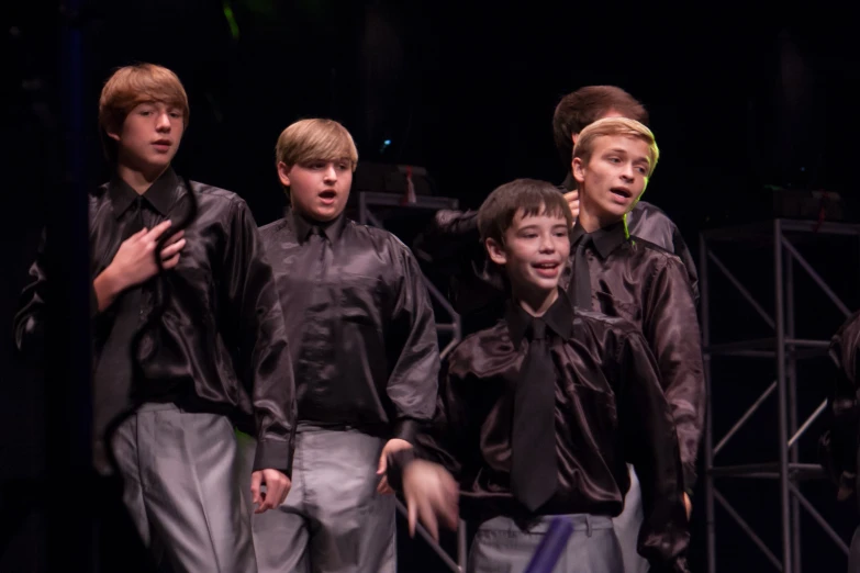 boys sing into microphones while performing on stage