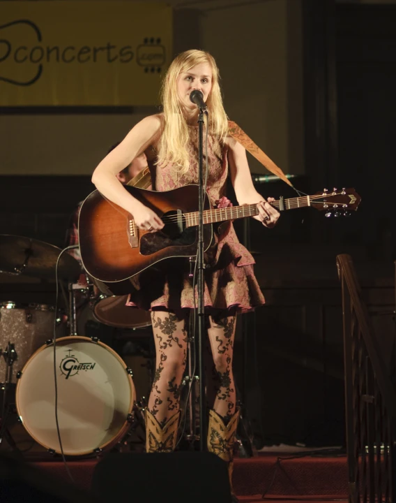 a beautiful young woman holding a guitar while standing on a stage