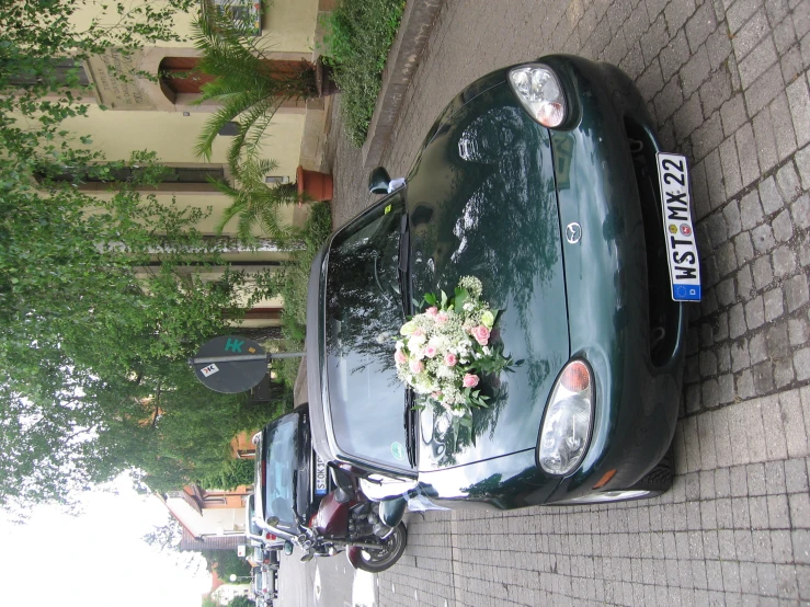 a car parked next to two motorcycles with a floral bouquet on the hood