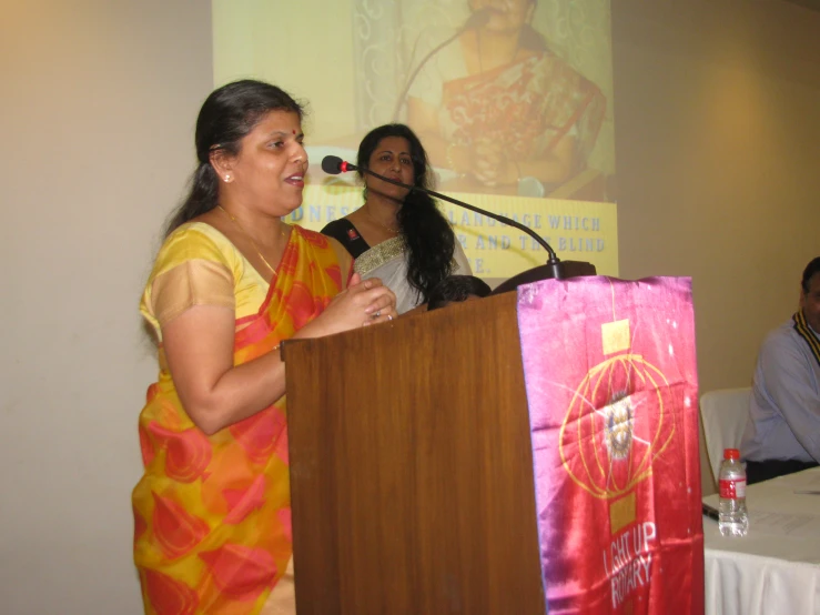 two women standing at a podium and speaking to the audience