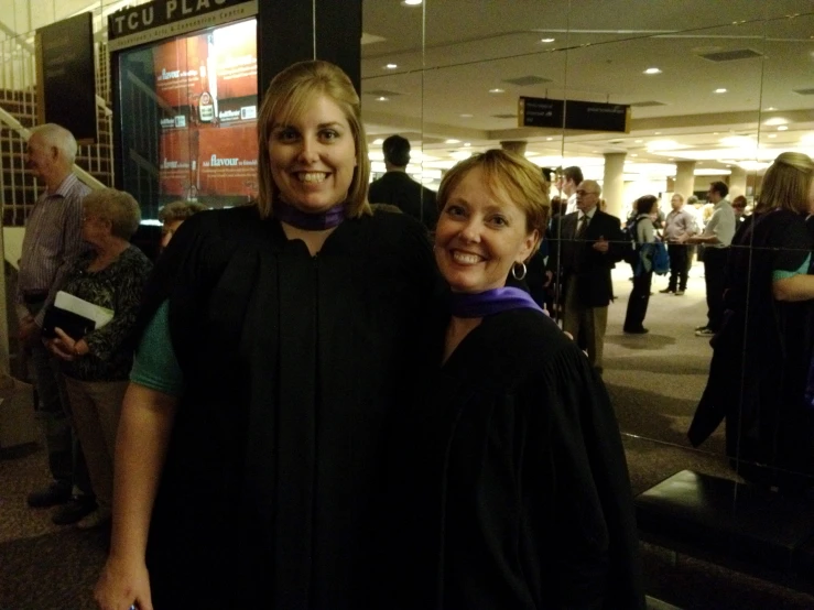 two women in graduation robes pose for a po