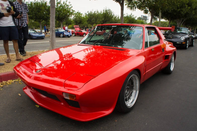 red classic car in parking lot with a man standing nearby