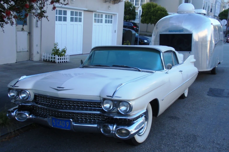 a white classic car parked in front of a silver trailer