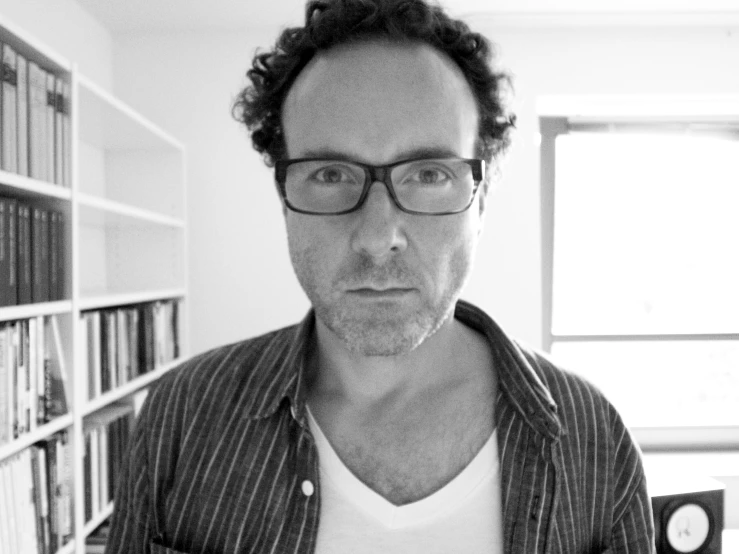 a man in glasses standing in front of bookshelves