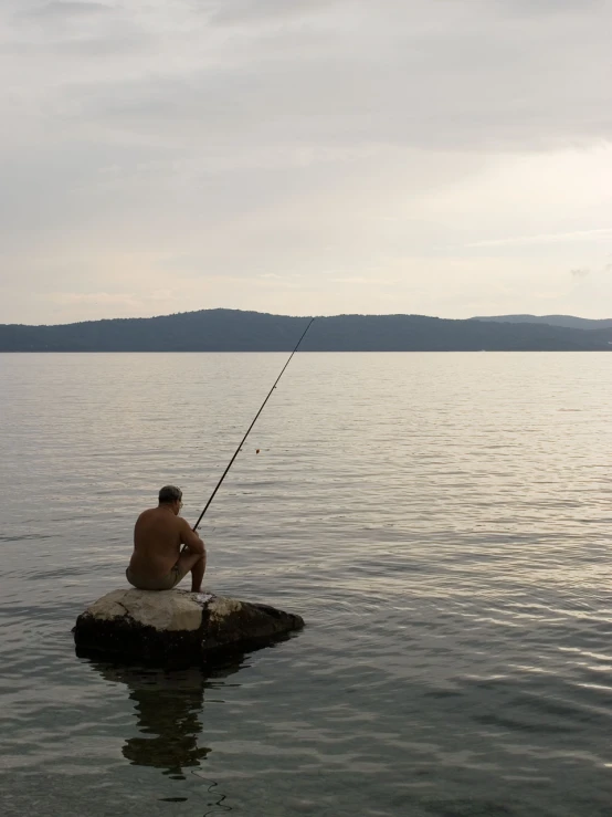 the man is fishing from a rock in the water