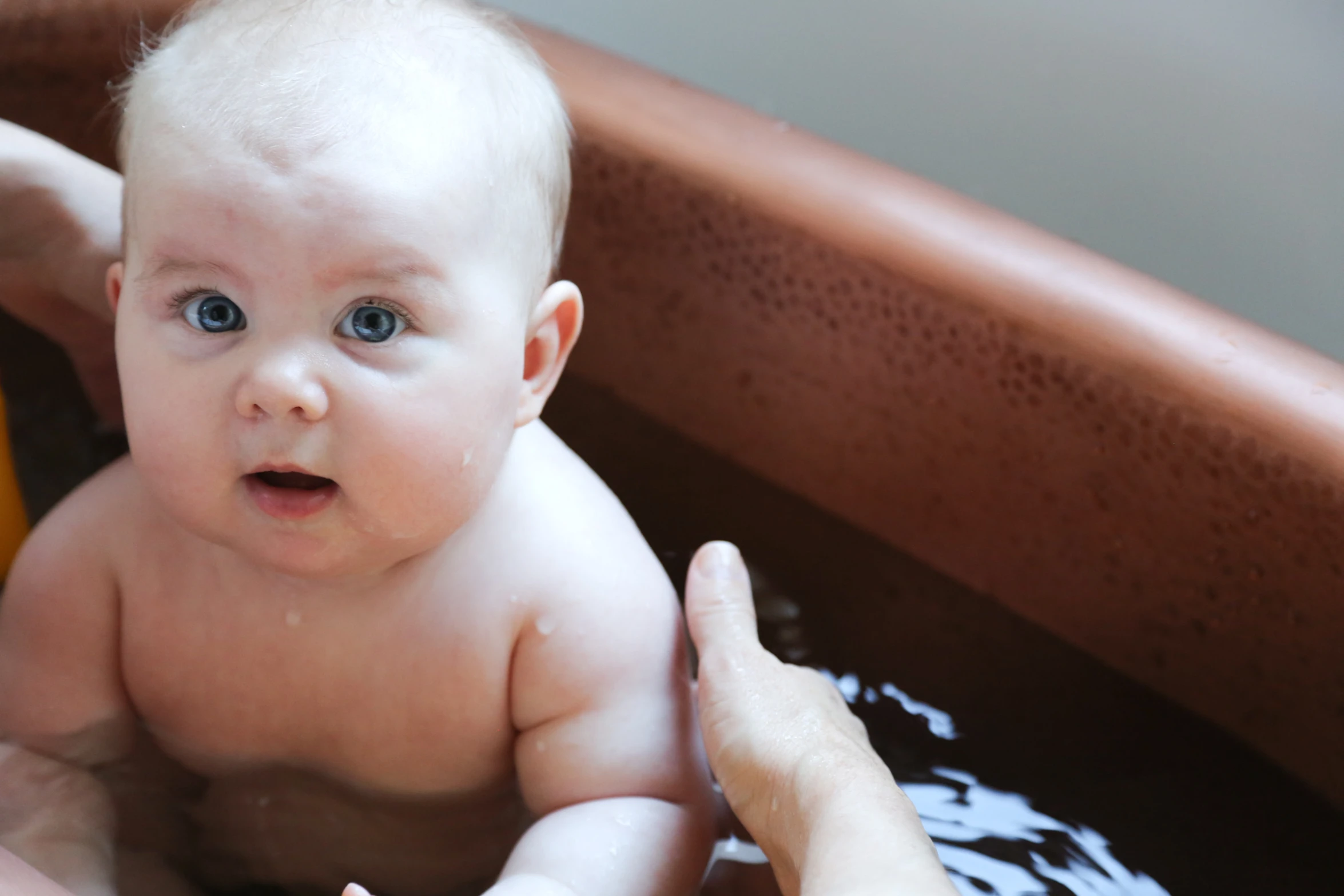 a baby in a basin being held by someone