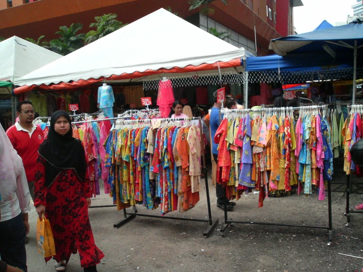 a woman with a black head scarf in front of several colorful shirts