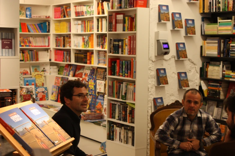 three men talking to each other in front of a book shelf