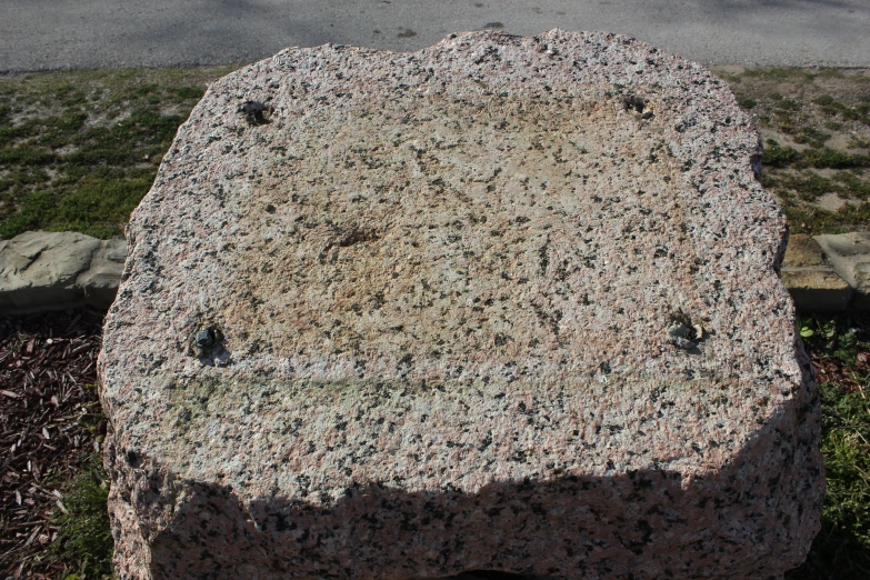 a big rock outside near the road and some grass